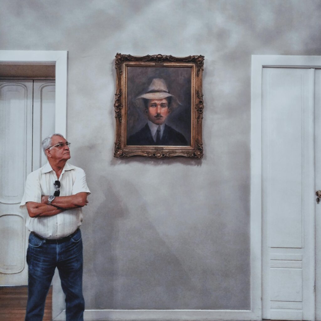 Man observing a framed painting in an indoor art gallery or museum setting.